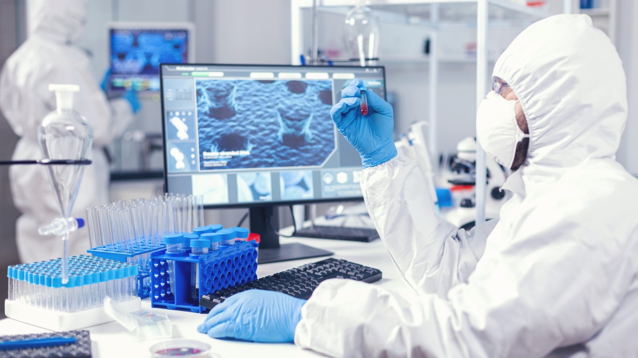 Scientist in protection suit holding sample of infected blood with coronavirus in test tube. Doctor working with various bacteria and tissue, pharmaceutical research for antibiotics against covid19.